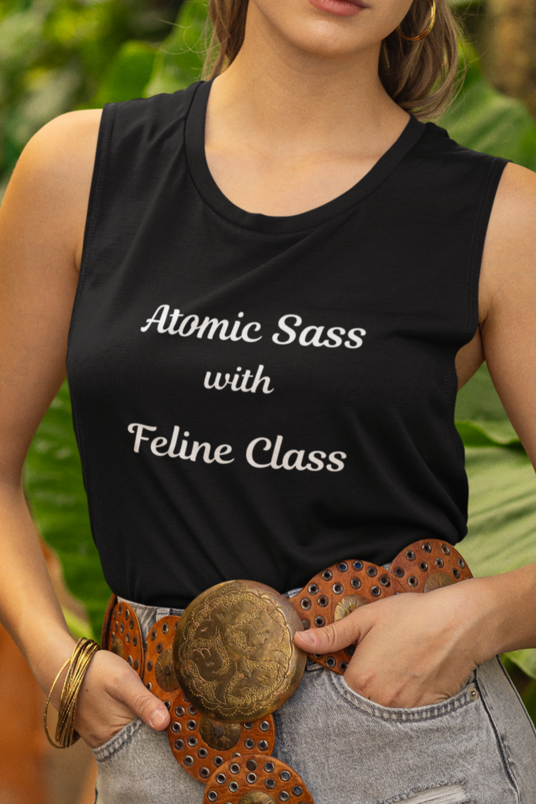 Woman wearing a black sleeveless shirt with text, denim shorts, and a hat in a garden setting.