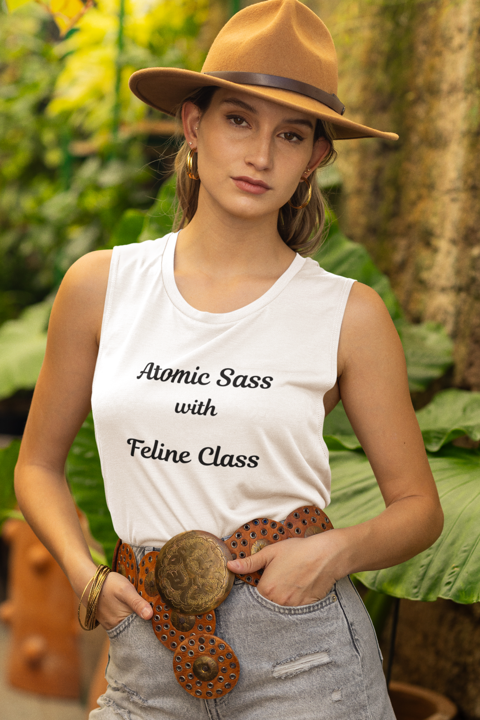 Woman wearing a white tank top with text, denim shorts, and a hat in a garden setting.
