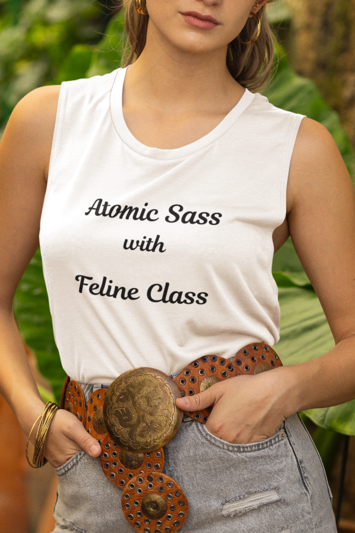 Woman wearing a white tank top with text, denim shorts, and a hat in a garden setting.