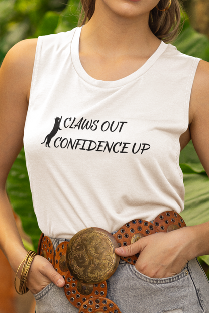 Woman wearing a white tank top with text, denim shorts, and a hat in a garden setting.