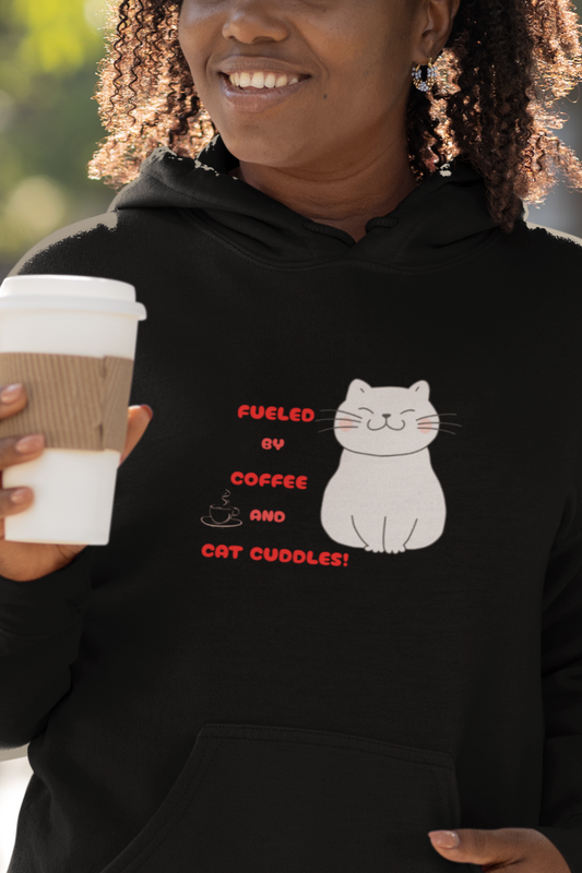 Woman wearing a black hoodie with a cat graphic and text, holding a coffee cup outdoors.