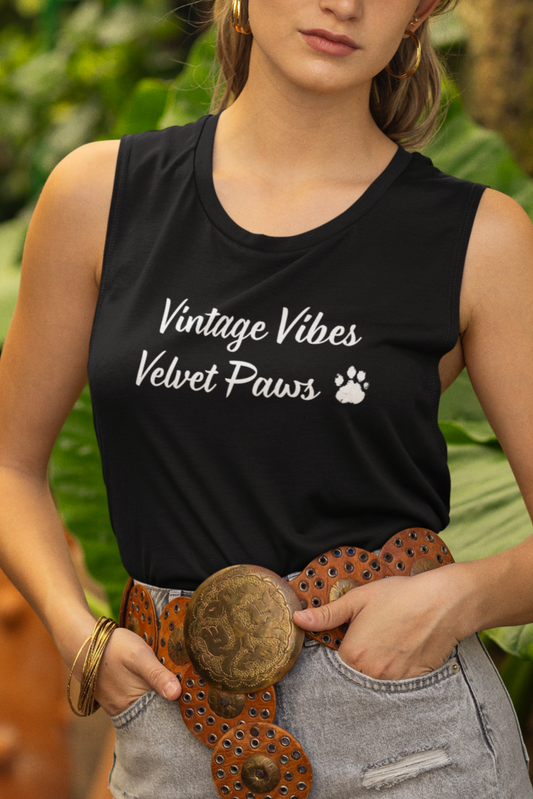 Woman wearing a black sleeveless shirt with text, denim shorts, and a brown hat in a garden setting.