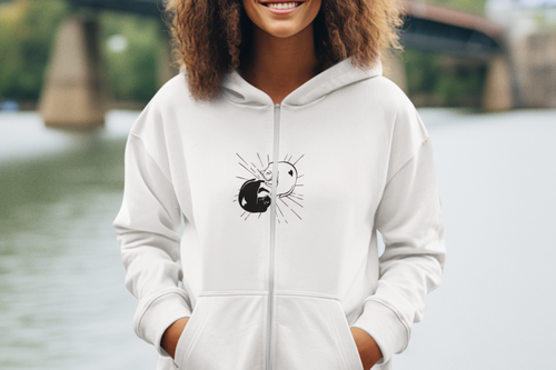 Person wearing a white hoodie with a spider design by a river