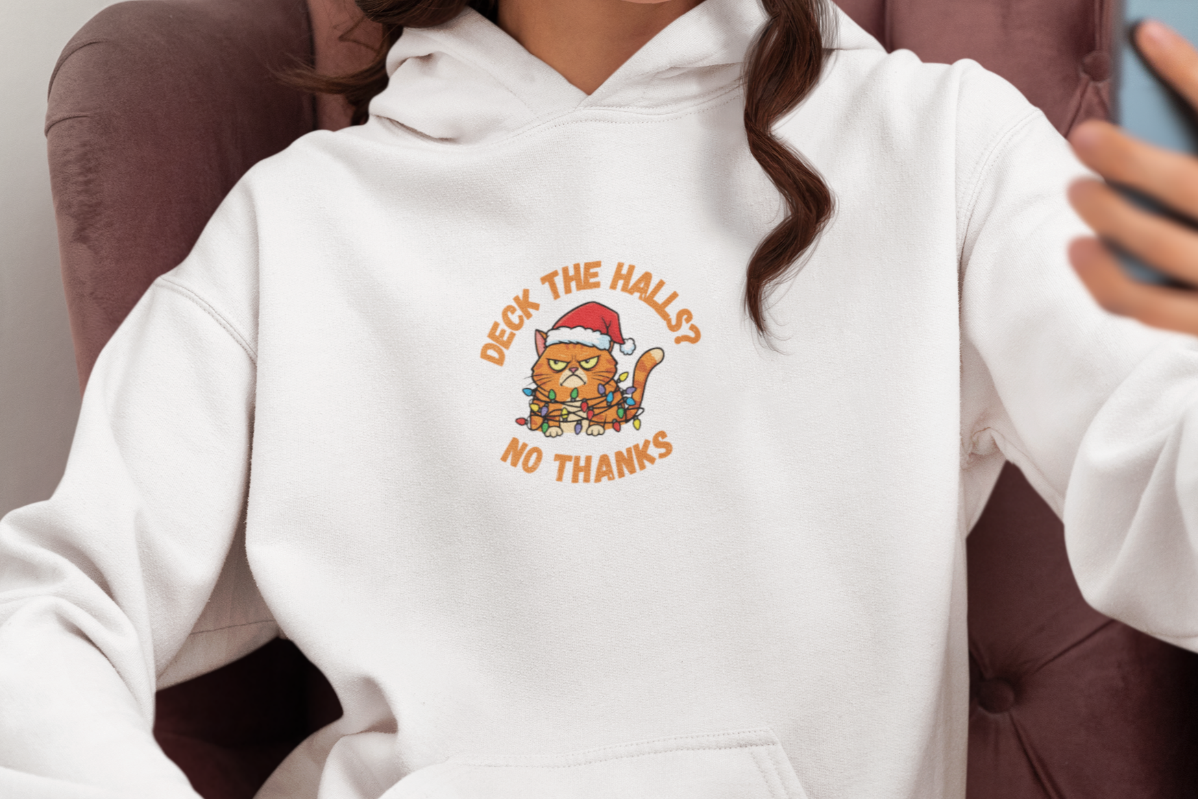 Person wearing a white hoodie with a graphic design, sitting in a chair and taking a selfie.