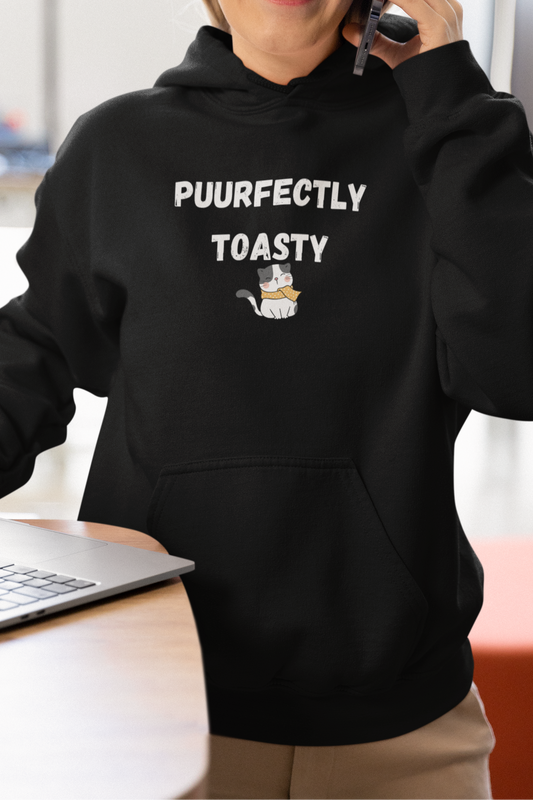Person wearing a black hoodie with text and a graphic, using a phone and laptop indoors.