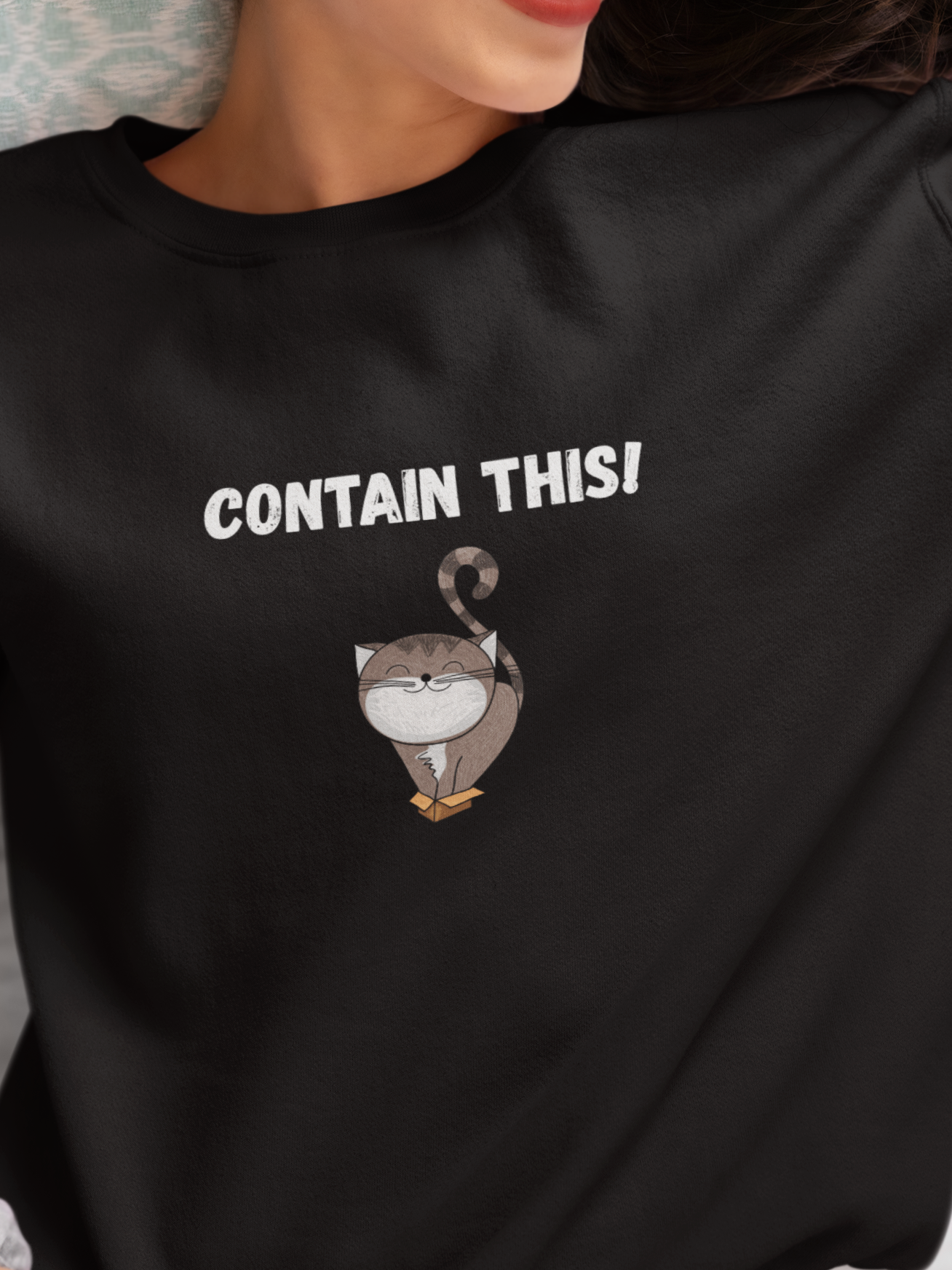 Person wearing a black sweatshirt with text and graphic design, sitting on a bed.