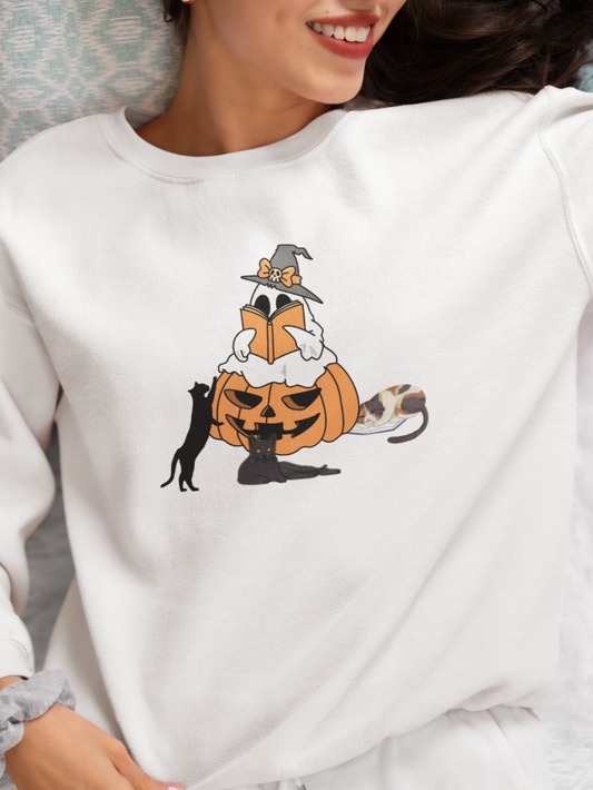 Person wearing a white sweatshirt with a Halloween-themed design featuring a pumpkin, cat, and raccoon.