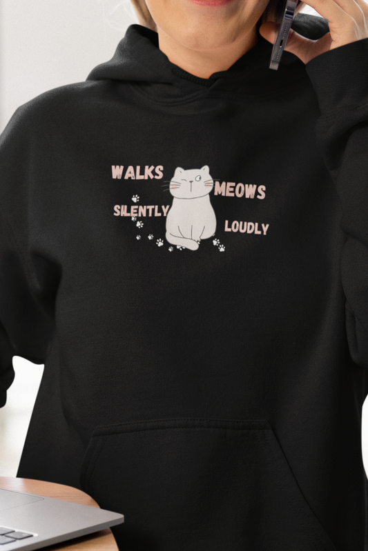 Person wearing a black hoodie with a graphic and text, using a phone indoors.