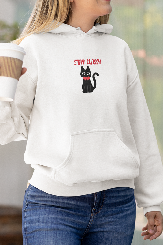 Woman wearing a white hoodie with a black cat design and text, holding a coffee cup outdoors.