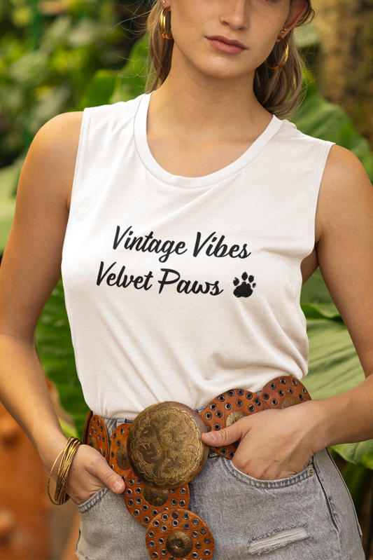 Woman wearing a white tank top with text, denim shorts, and a hat in a garden setting.